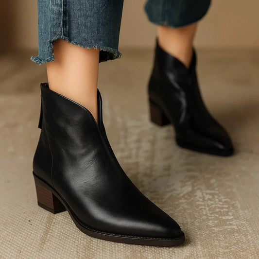 Black pointed-toe ankle boots with angled openings and low block heels, styled with cropped jeans.