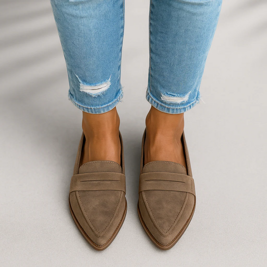 Taupe pointed toe slip-on loafers worn with light blue cropped jeans, shown from above with layered upper detailing.