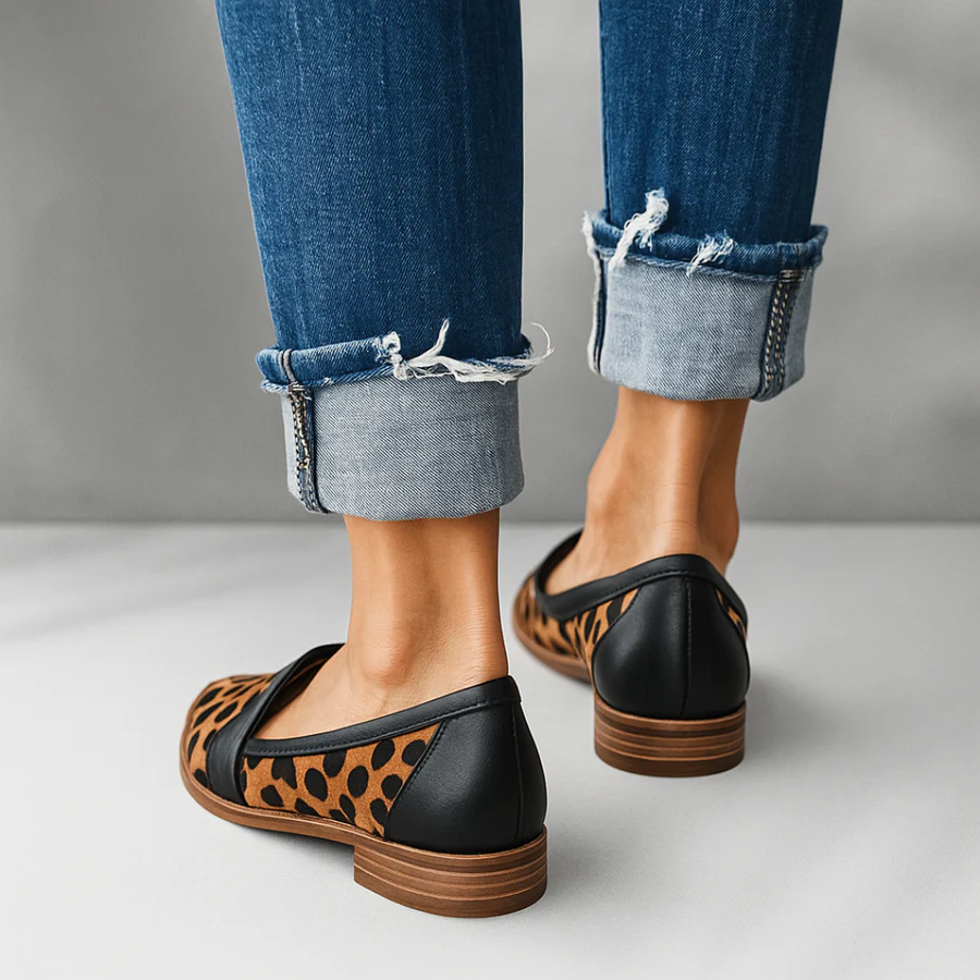 Rear view of leopard-print loafers with black heel panels and stacked low soles, worn with cuffed jeans.