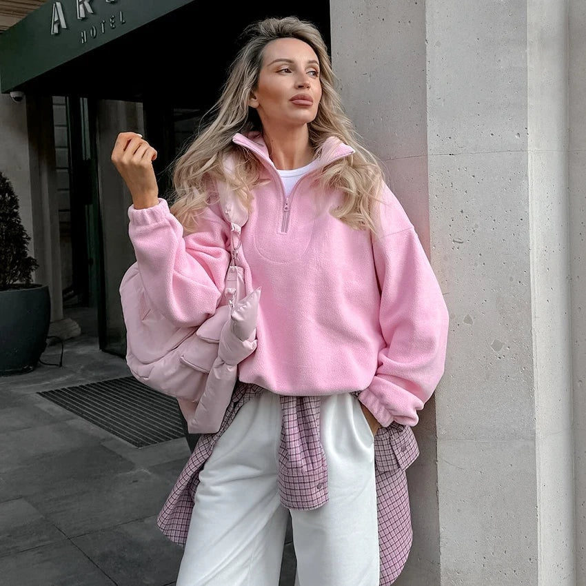 Model wearing the pink quarter-zip sweatshirt open at the collar with white trousers and a checked shirt tied at the waist.