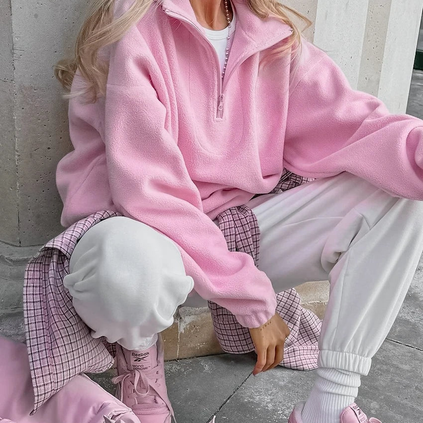 Seated model wearing the pink quarter-zip sweatshirt with the sleeves pulled toward the wrists and the collar open.