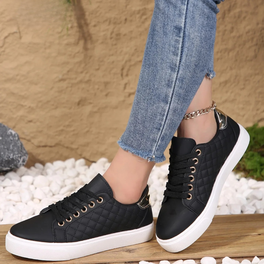 Black quilted low-top lace-up sneakers with metallic eyelets and heel accents, posed on a wooden surface.