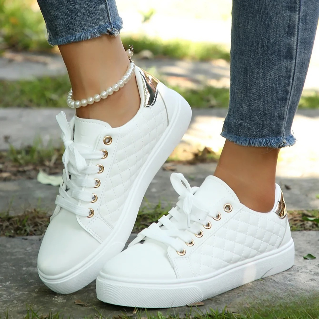Pair of white quilted sneakers viewed from the side, highlighting their textured panels, round toes, and metallic heel details.