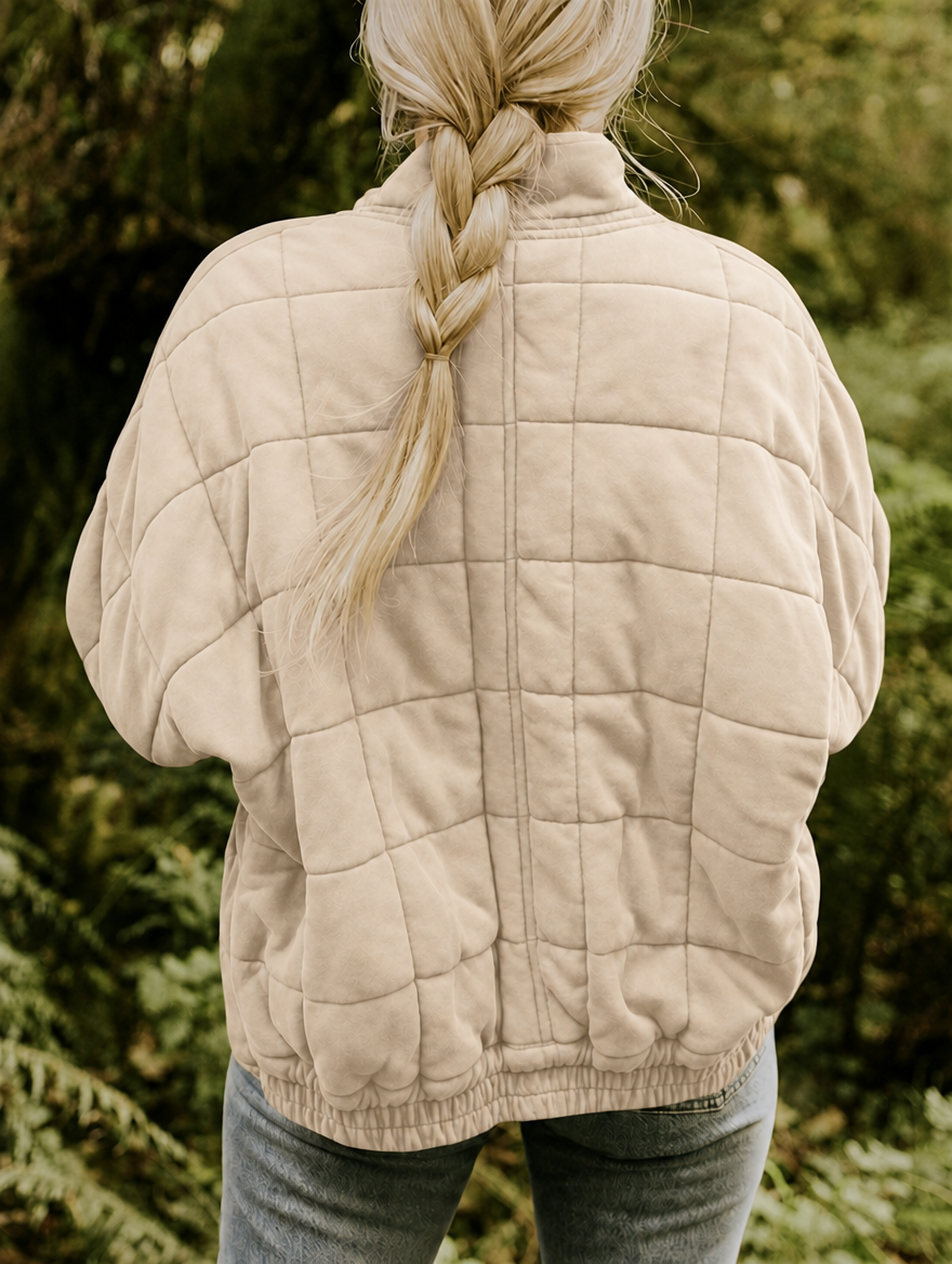 Back view of the light neutral quilted jacket with a relaxed silhouette, geometric stitching, and gathered hem.