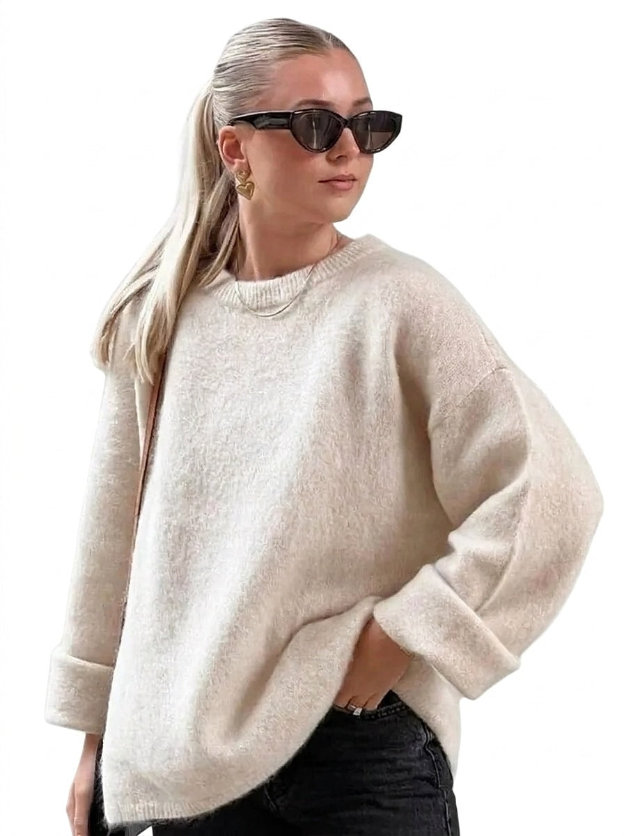 Cream relaxed crew-neck sweater styled with dark jeans, showing dropped shoulders, long sleeves, and wide turn-up cuffs.