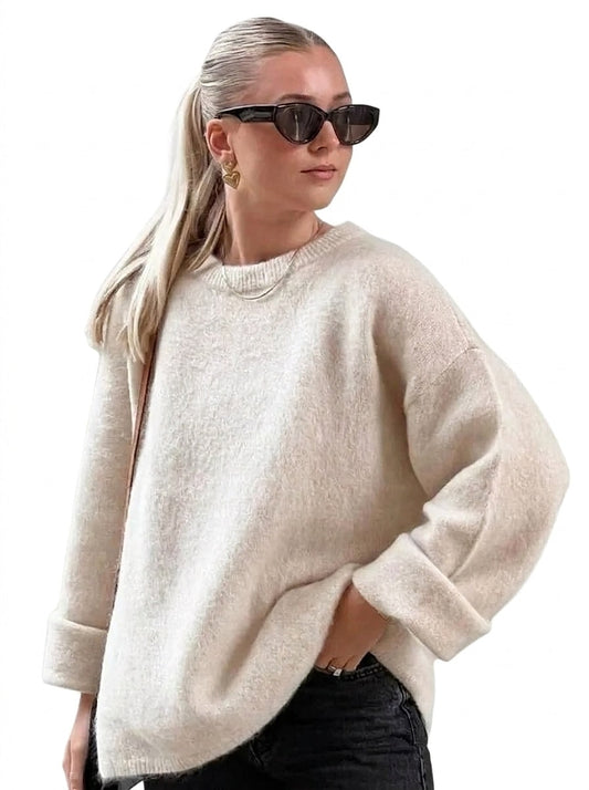Cream relaxed crew-neck sweater styled with dark jeans, showing dropped shoulders, long sleeves, and wide turn-up cuffs.