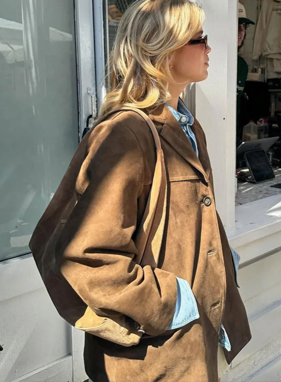 Side view of the brown relaxed blazer showing its roomy long sleeve, notch lapel, button closure, front pocket, and straight hem.