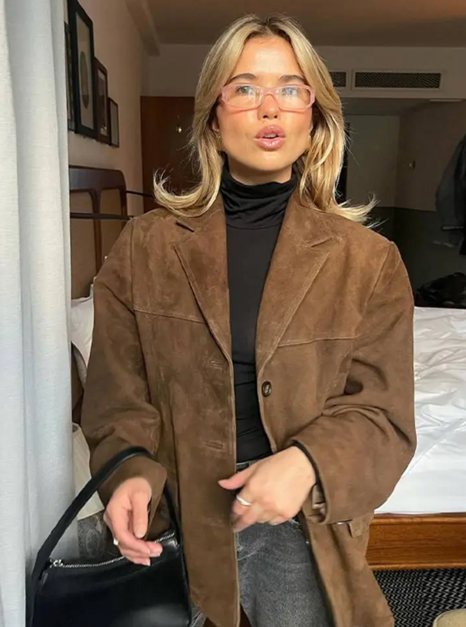 Brown single-breasted blazer styled over a black top, shown from the front with notch lapels, long sleeves, a button closure, and front pockets.