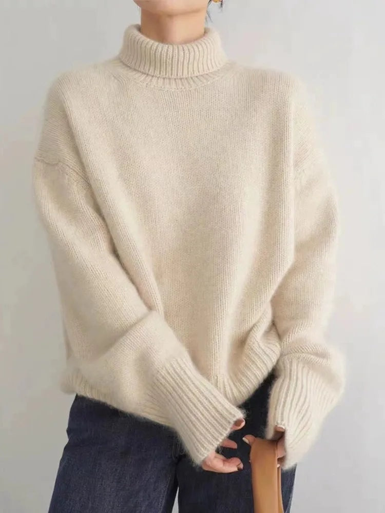 Front view of a cream relaxed-fit turtleneck sweater with dropped shoulders and extended ribbed cuffs, paired with dark jeans.