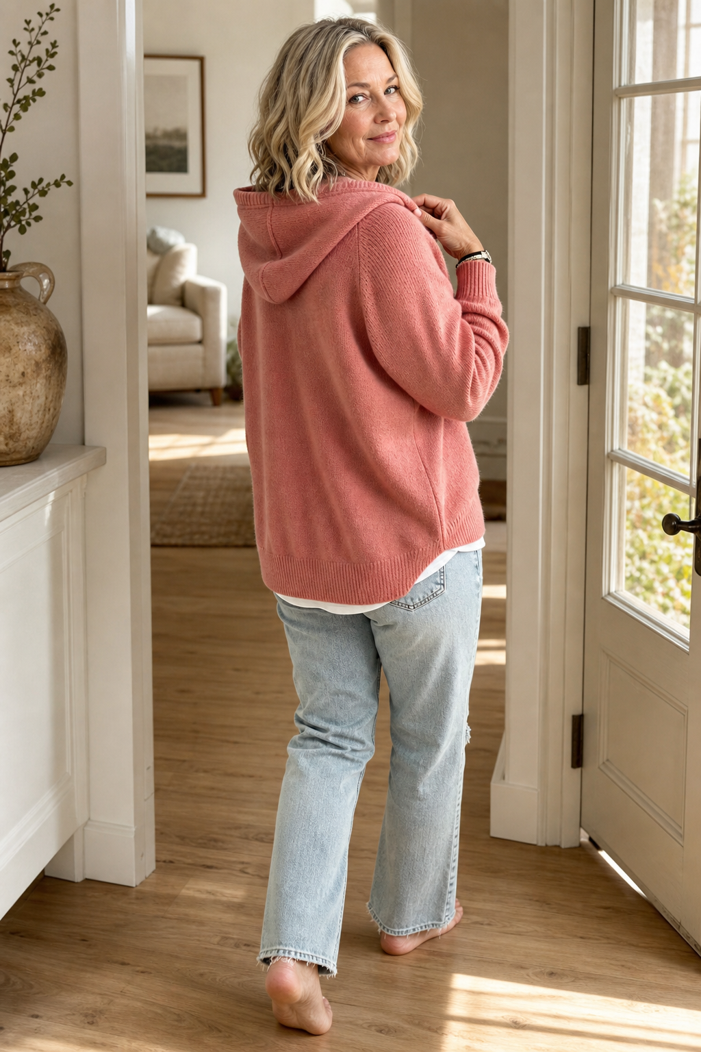Back and side view of the pink pullover, highlighting the hood and ribbed hem as the wearer walks away.