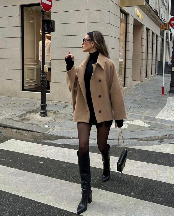 Model wearing a camel short oversized coat with a point collar and button front while crossing a city street.