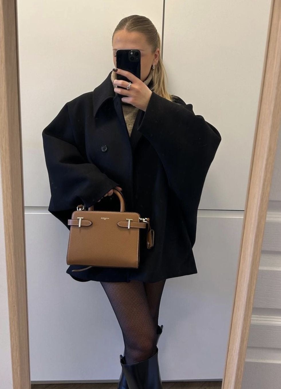 Mirror view of the black coat highlighting its oversized sleeves, point collar, and front button closure.