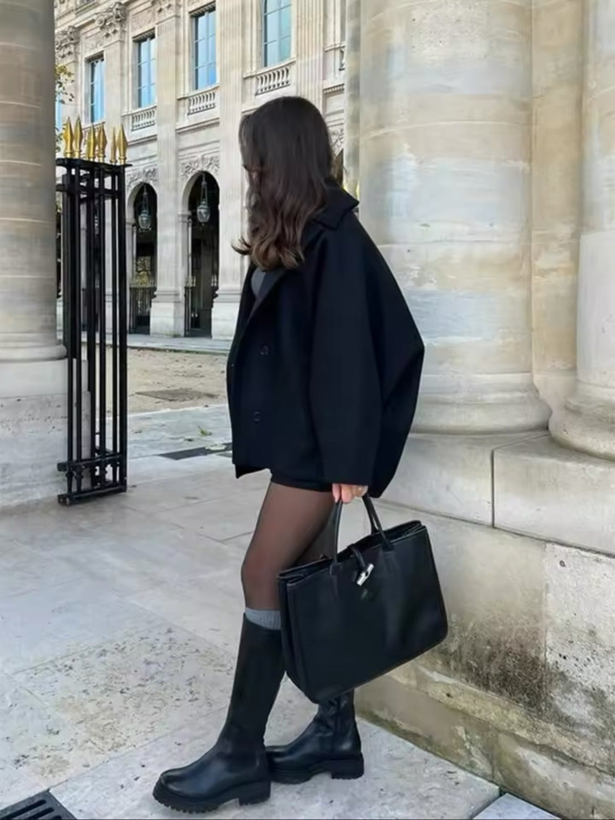 Side view of the black short coat showing its roomy straight silhouette, long sleeve, and buttoned front.