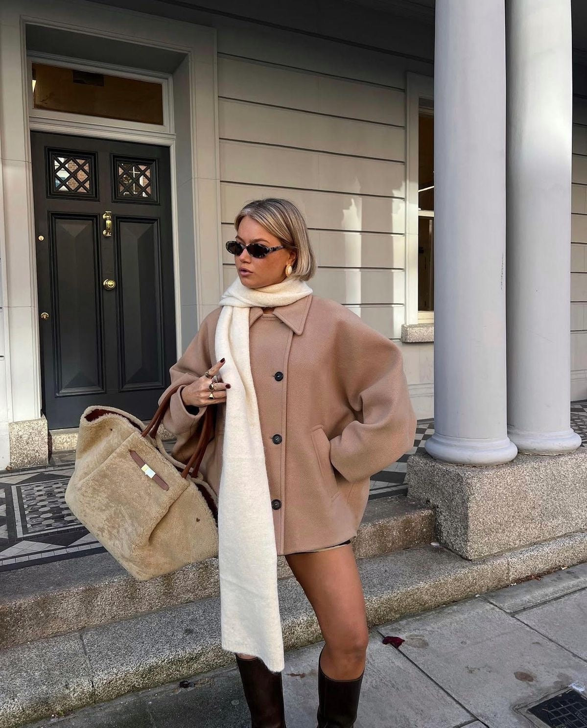 Model wearing the camel coat buttoned with a long scarf, showing the pointed collar and short hemline.