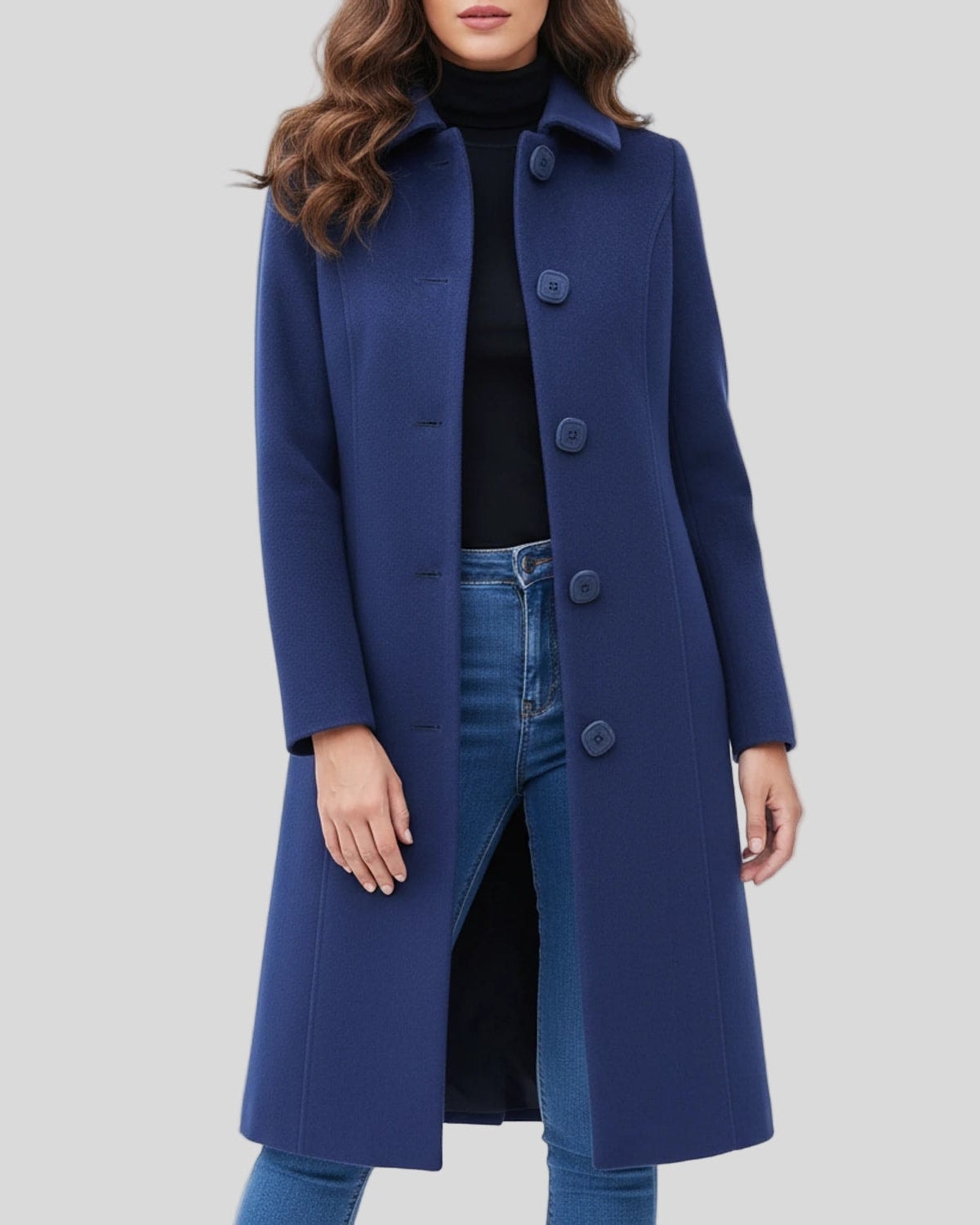 Blue single-breasted knee-length coat with a stand collar, long sleeves, and gently shaped fit, styled over a black top and jeans.