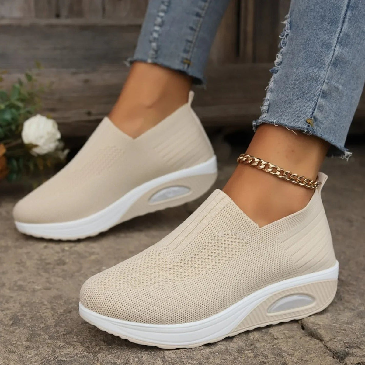 Beige slip-on platform sneakers worn outdoors, with textured uppers, white raised soles, and oval side accents visible.
