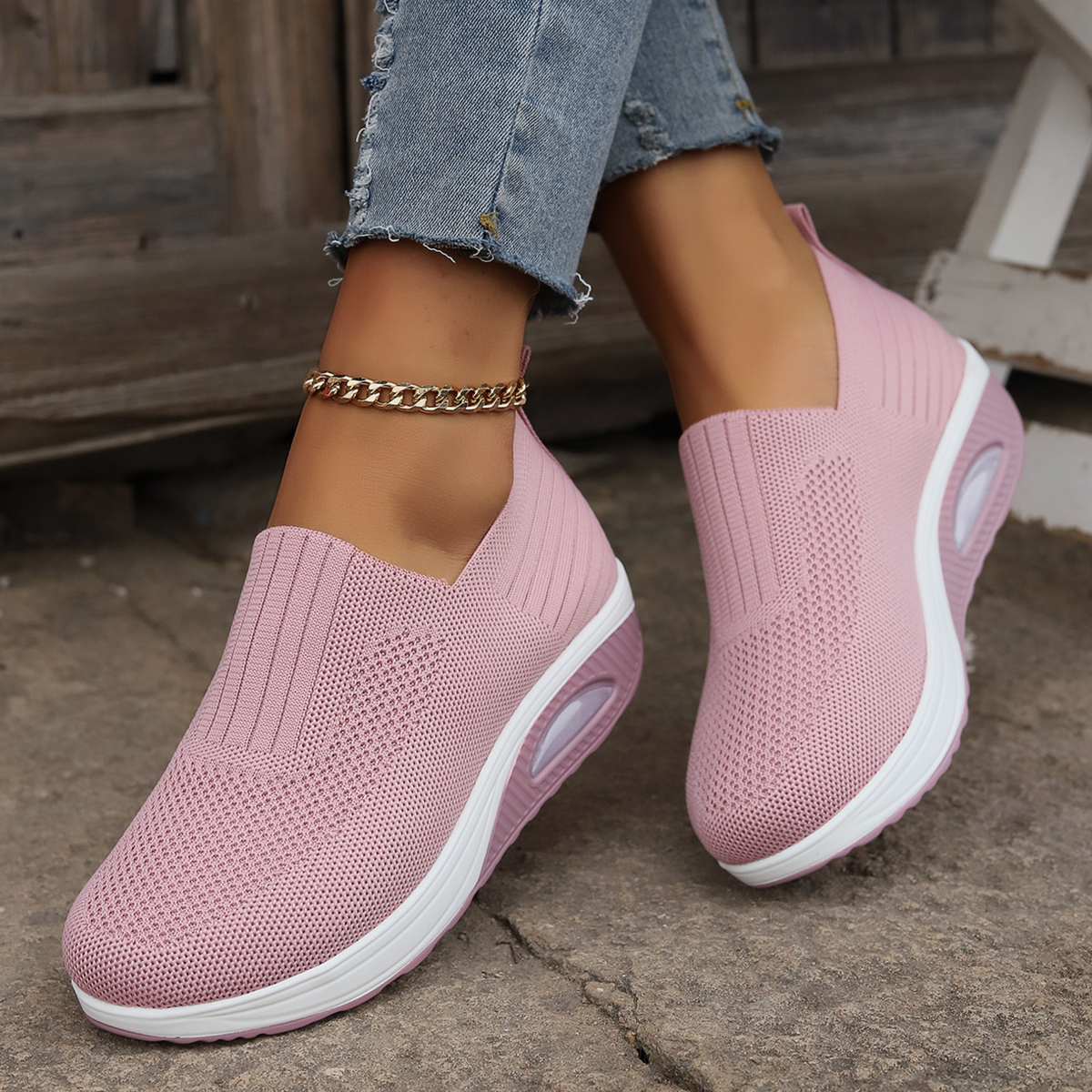 Pink slip-on platform sneakers worn on a stone surface, showing their textured uppers and pink raised soles from the front and side.
