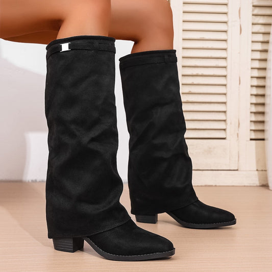 Black slouch knee-high boots with gently tapered toes and low block heels, shown standing on a wood floor.