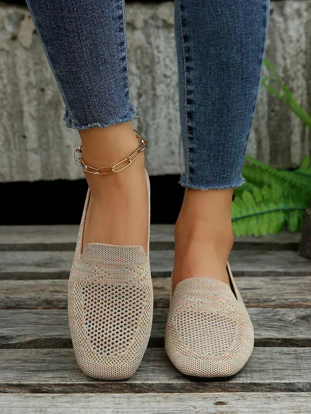 Pair of beige open-knit square-toe flats worn with jeans and shown from the front on a wooden bench.