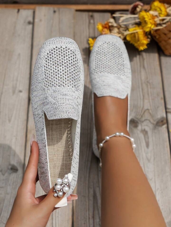 Light gray open-knit square-toe flat held beside a matching worn flat on a wooden surface.