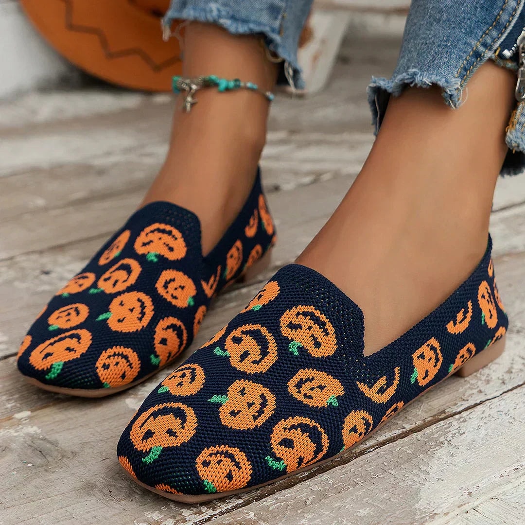 Navy slip-on flats decorated with orange pumpkin motifs, shown from an angled front view with rounded square toes.