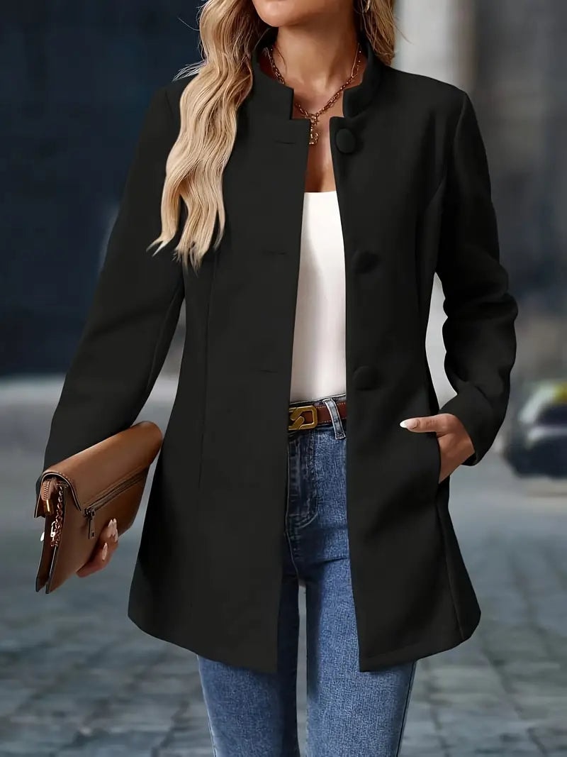 Black coat worn open from the front with one hand in a pocket and a clutch in the other.