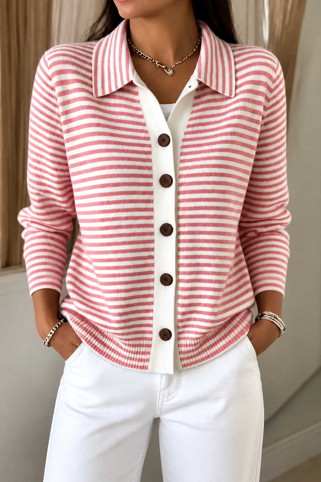 Front view of the pink-and-white striped cardigan styled with white trousers and hands in pockets.