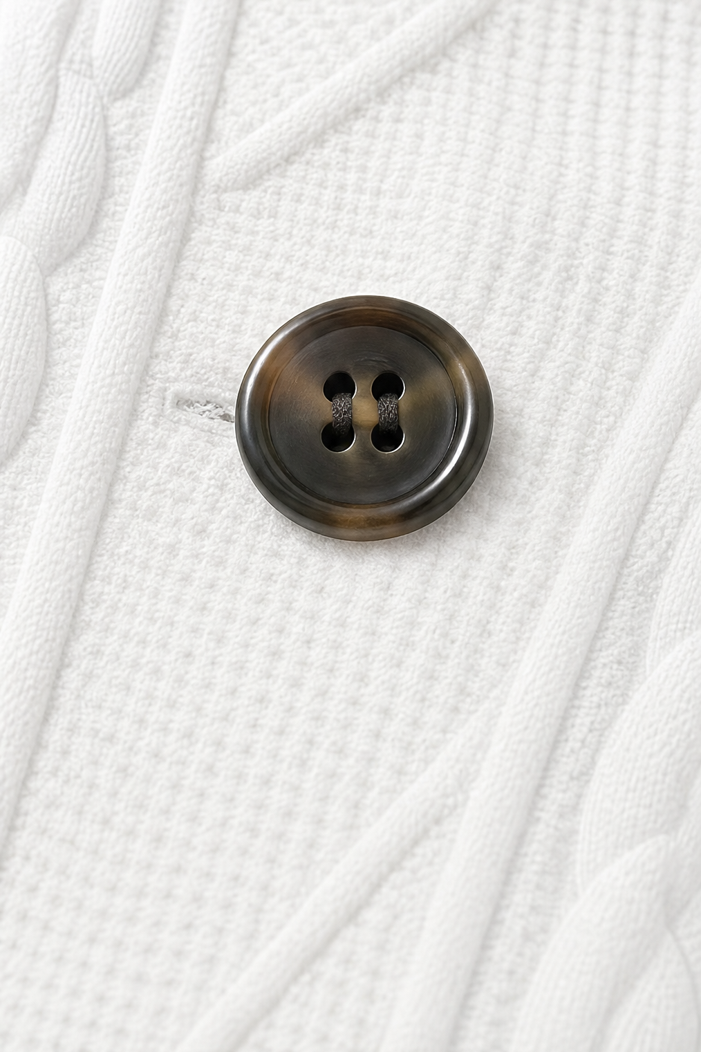Close-up of a dark four-hole button set against the blazer’s white textured front.