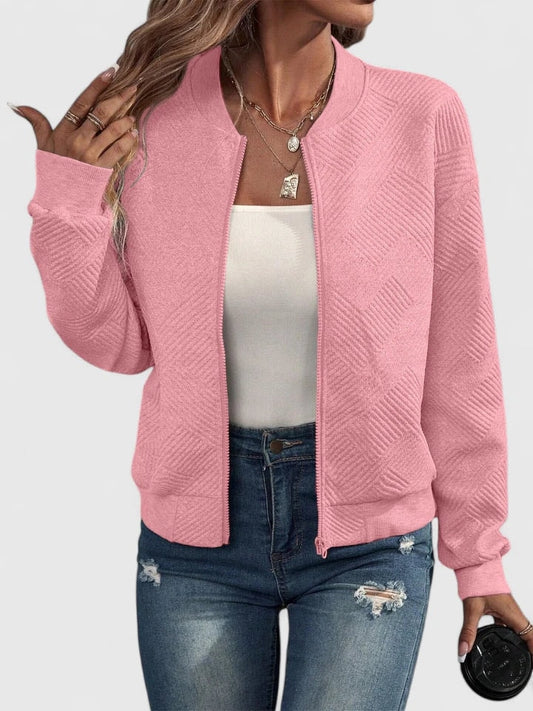 Pink textured geometric-pattern bomber jacket with a round neckline, zip front, long sleeves, and waist-length fit, styled with a white top and distressed jeans.