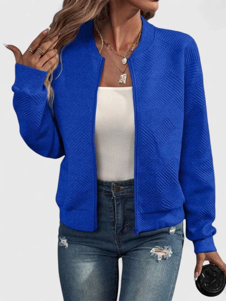 Bright blue textured bomber jacket featuring a round neckline, full-length zipper, long sleeves, and ribbed cuffs, worn over a white top.