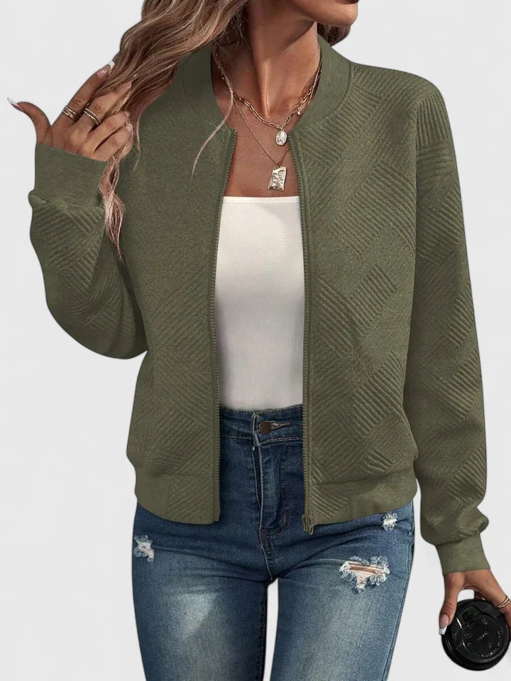 Olive green textured zip-up bomber jacket with long sleeves and a clean round neckline, styled with a white top and distressed denim.