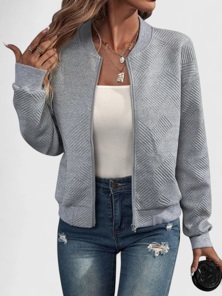 Gray textured geometric-pattern jacket with a round neckline and full-length zip front, worn over a white top and blue jeans.