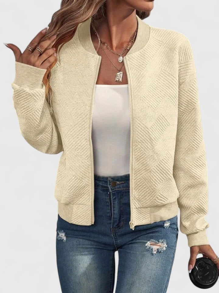 Cream textured zip-up bomber jacket with a geometric pattern, round neckline, long sleeves, and ribbed hem, layered over a white top.