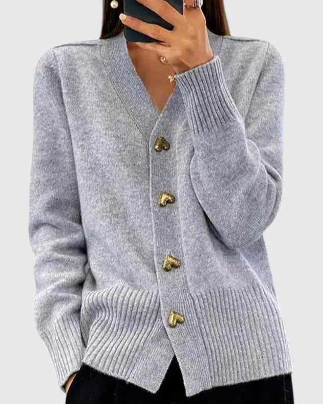 Light gray V-neck cardigan featuring four heart-shaped front buttons and wide ribbed trim, paired with black trousers.