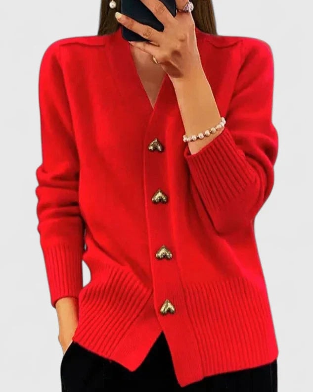 Bright red V-neck cardigan with heart-shaped buttons and ribbed trim, worn with black trousers.