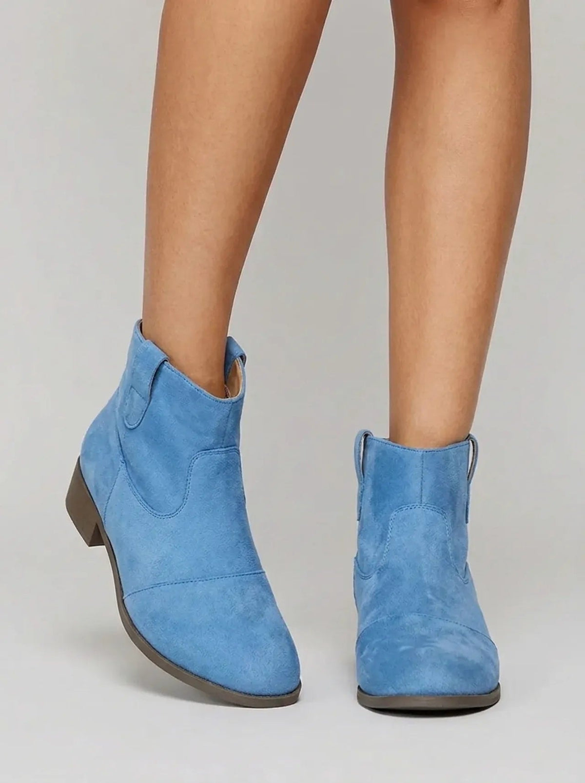 Three-quarter front view of blue Western ankle boots highlighting the curved shaft openings, stitching, and practical low heels.