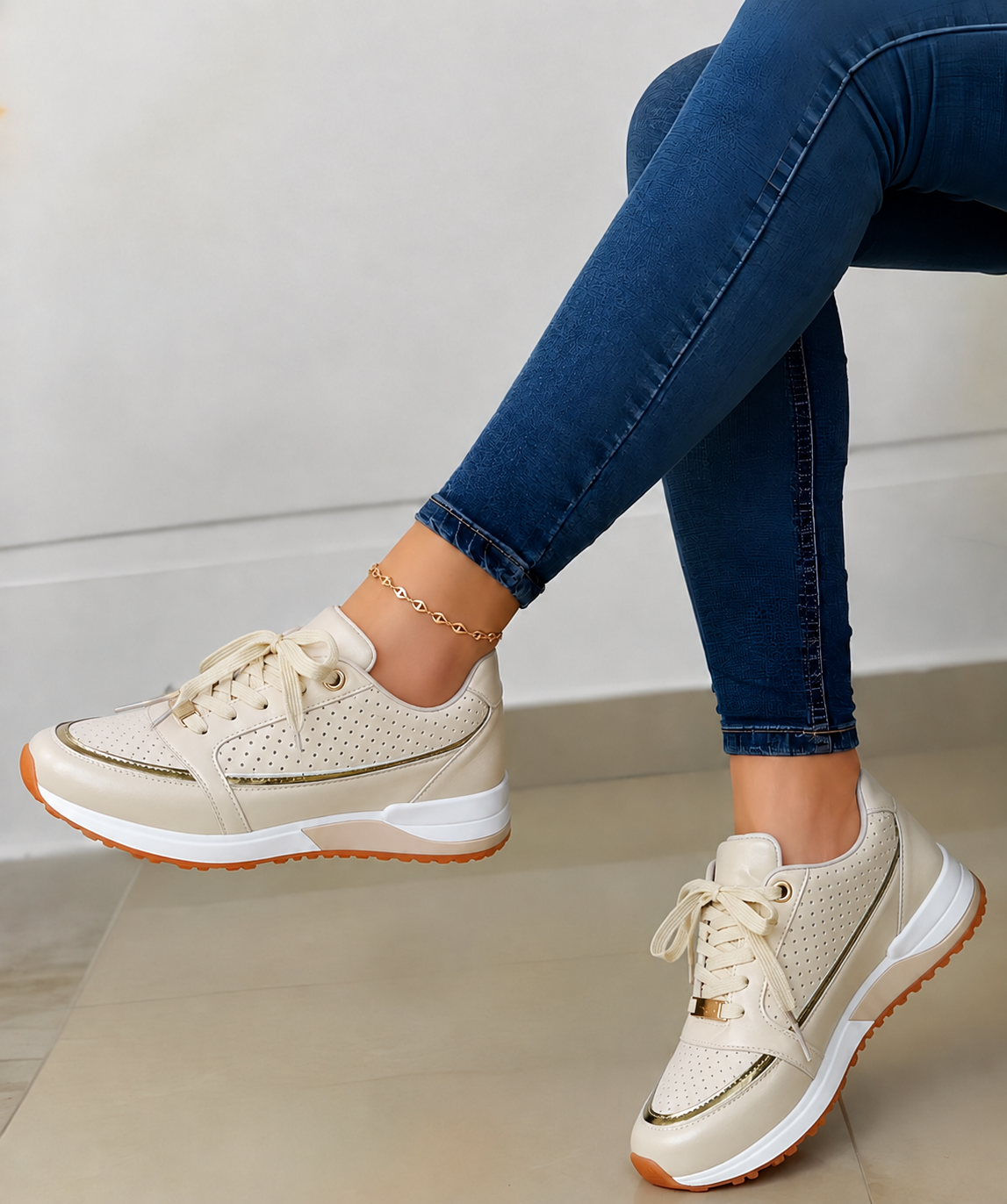 Cream low-top women's lace-up sneakers with perforated side panels, matching metallic trim, and a contrasting brown-edged sole.