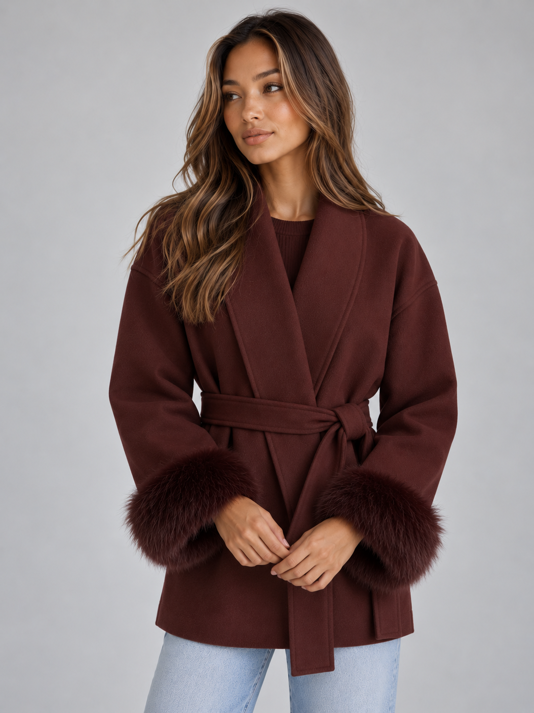 Front three-quarter view of the wrap coat in burgundy, showing the tied belt, overlapping front, relaxed sleeves, and dark plush cuffs.